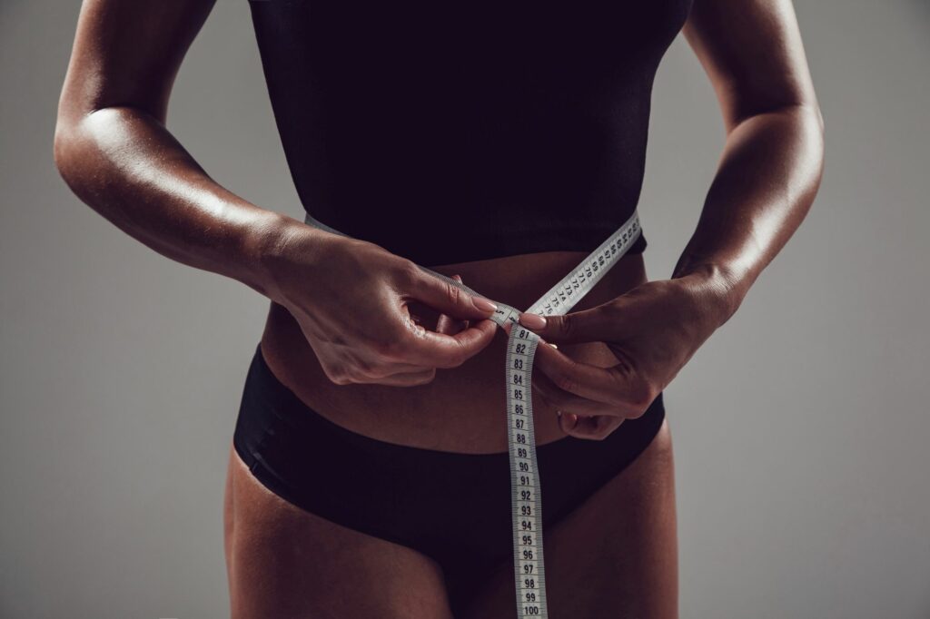 Athletic slim woman measuring her waist with measuring tape | Odomí Medical Spa in Savannah, GA